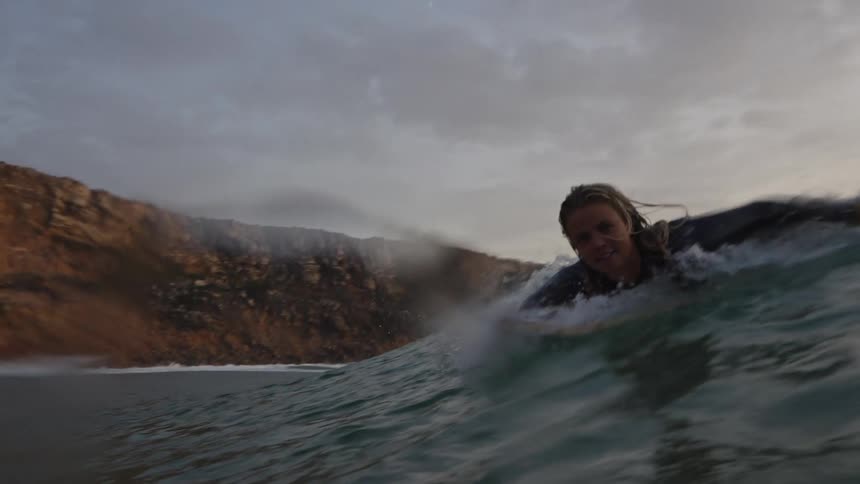 Surfer paddling on a wave near a cliff
