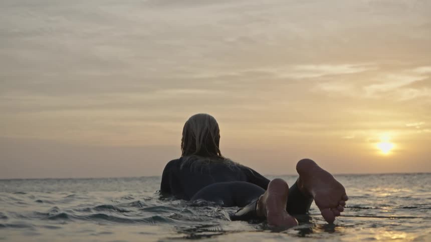 Two surfers lying on their boards watching the sunset at sea