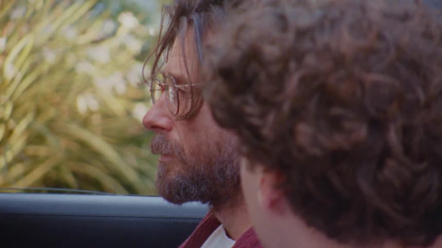 Bearded man wearing glasses seen in profile next to another person