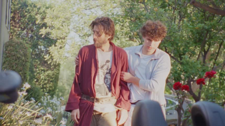 Man helping another walk through a garden