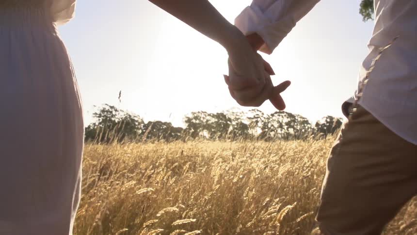 Couple walking through a field holding hands with sunlight between them