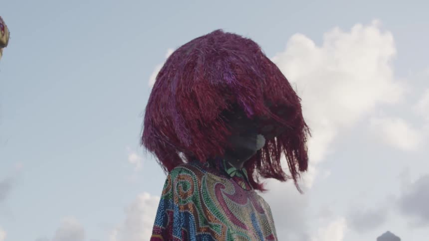 Giant puppet wearing colorful clothing and a red fringed hat