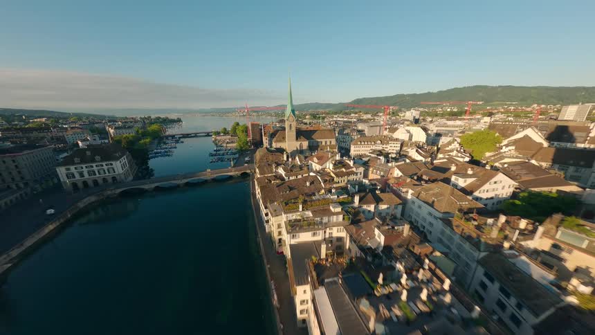 An aerial view captures the city of zurich with its distinctive grossmünster church the limmat river and lake zurich in the background all under a clear blue sky