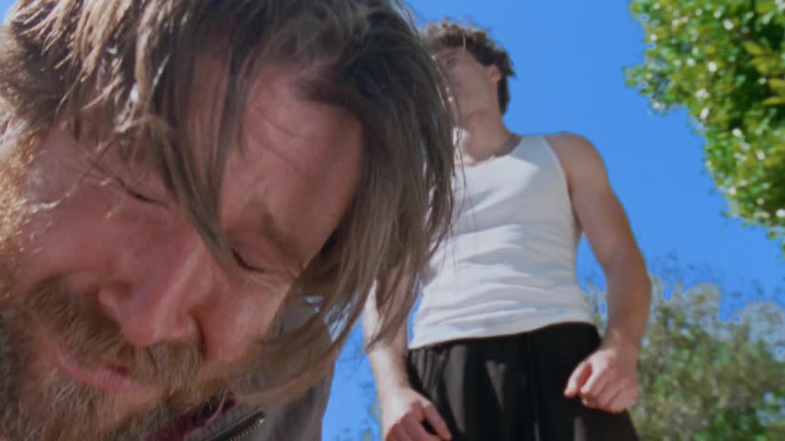 Bearded man in the foreground looks worried while another with hands on his hips watches him under a blue sky