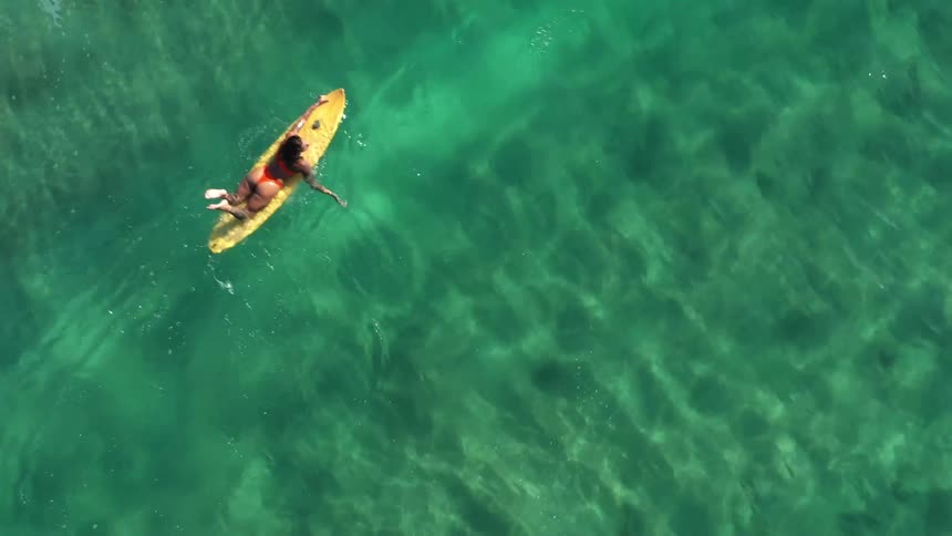 Person lying on a yellow surfboard paddles in the clear green sea