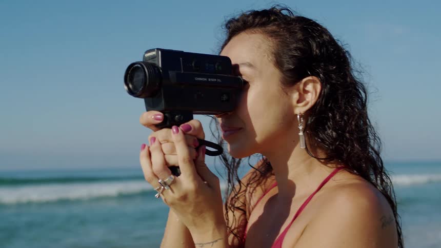 Woman in a red bikini films with a vintage camera by the sea
