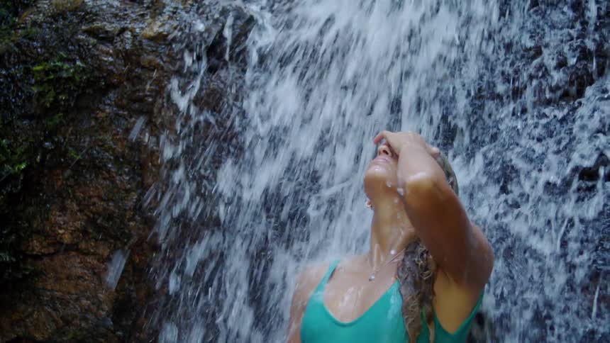 The woman stands under the waterfall