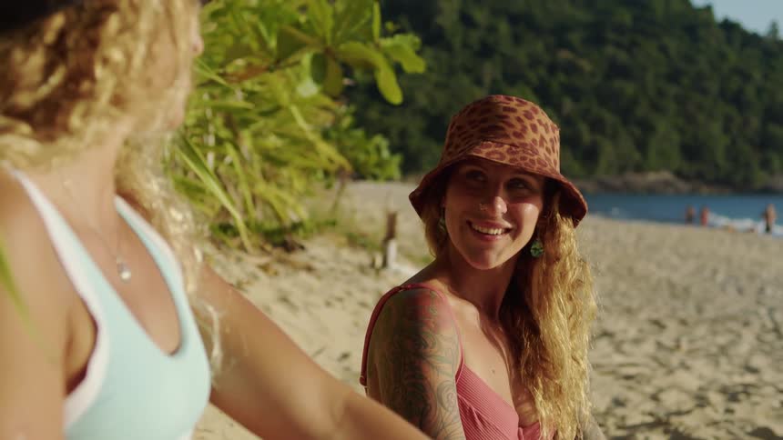 Two women sit on the beach during a vacation having a discussion and looking happy wearing swimsuits at midday