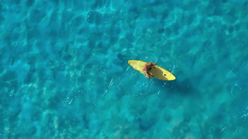 Woman in red bikini paddling on a yellow surfboard over crystal blue sea