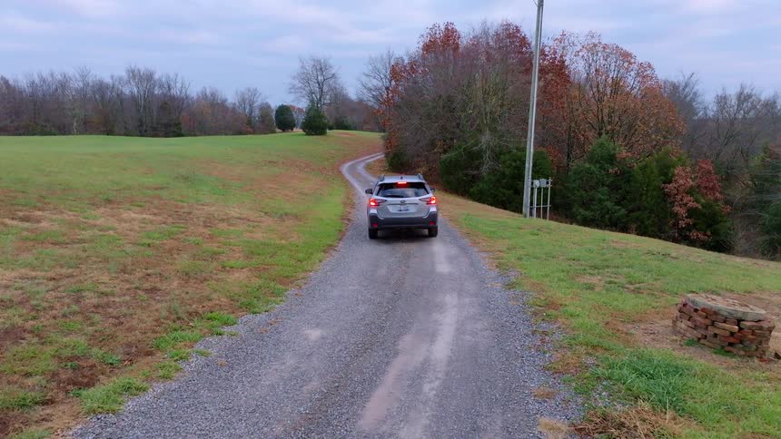 A car drives on a gravel road through a rural area