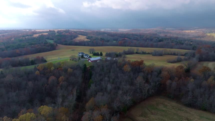 Aerial view of a rural landscape with rolling hills scattered trees in autumn colors and a farmhouse at the center