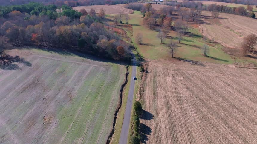 An atv driving on a road across tree plains and crop fields