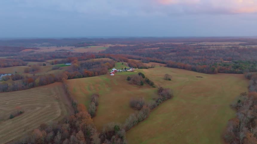 Isolated farm appears among fields and hills in an autumn landscape