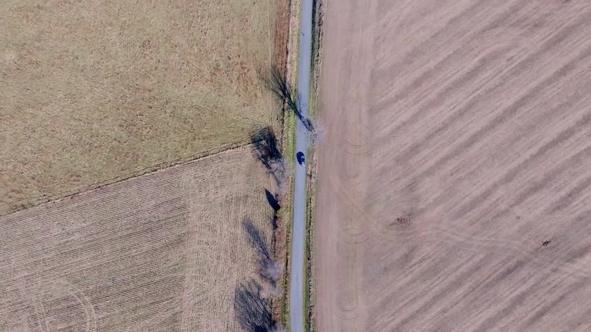 Car drives along a narrow road between two agricultural fields