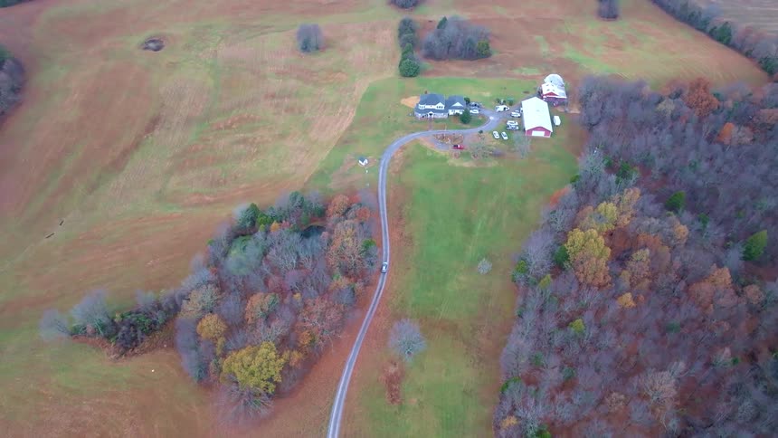 Aerial of a car driving along a rural road toward a farmhouse on an autumn day