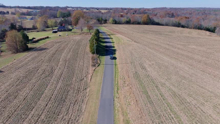 A car is driving down a road in between plowed fields