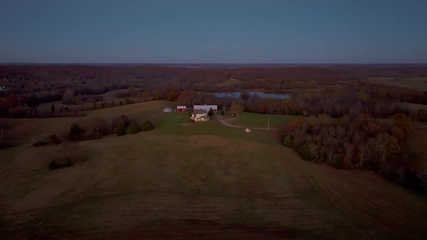 Farmhouse surrounded by fields and trees seen from above
