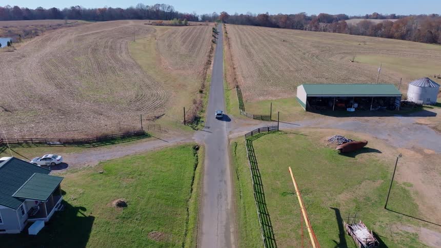 Car driving on a rural road surrounded by harvested fields houses and barns