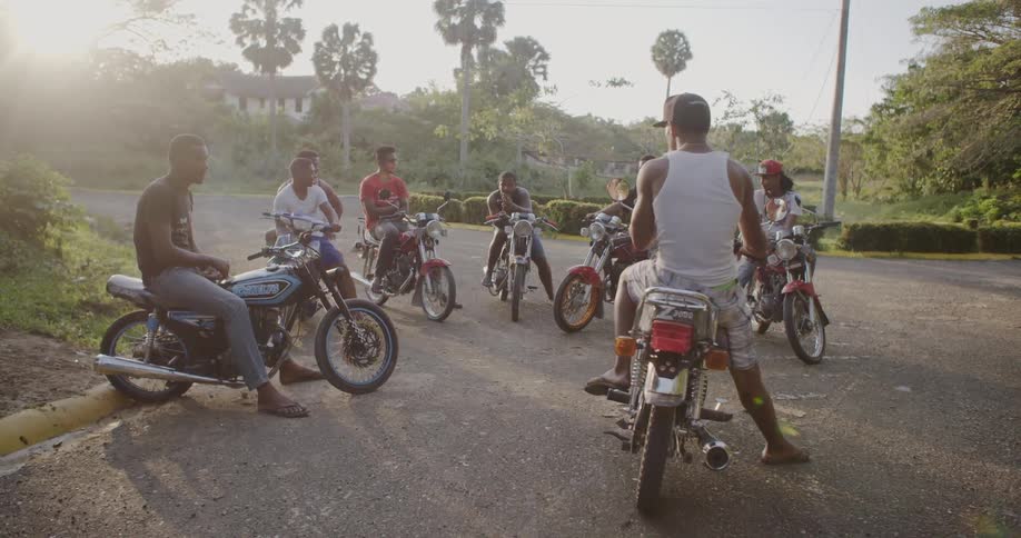 Men on motorcycles huddle together and smoke cigarettes