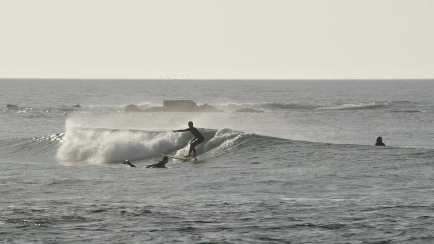 Surfer standing on the board rides a wave while others wait
