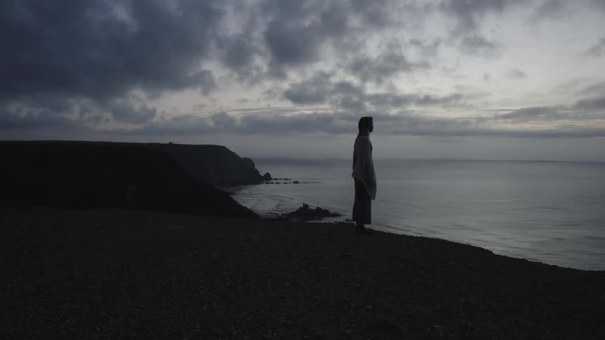 Person watches the sea at dusk from a cliff
