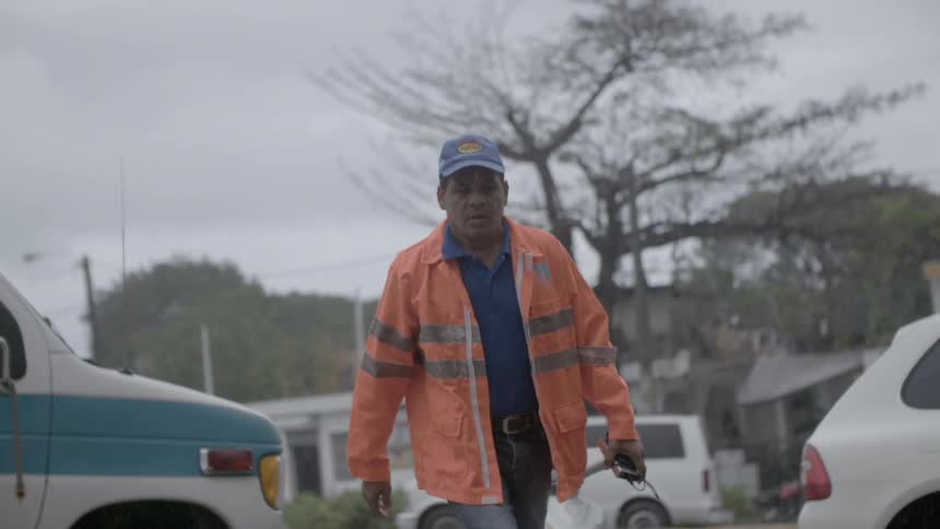 A man wearing an orange jacket walks across the street