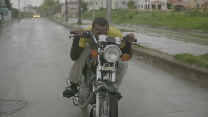 A man rides a motorcycle in a town setting while it rains