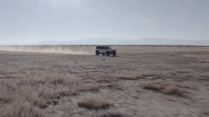 Offroad vehicle kicks up dust while crossing a dry field