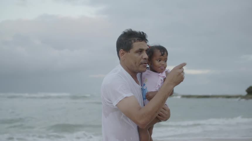 A man walks with a toddler on a beach