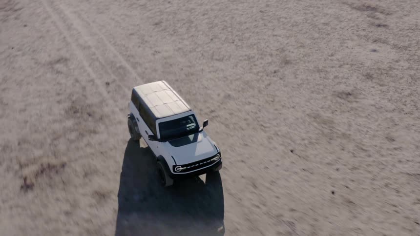 White suv drives across arid terrain casting a long shadow