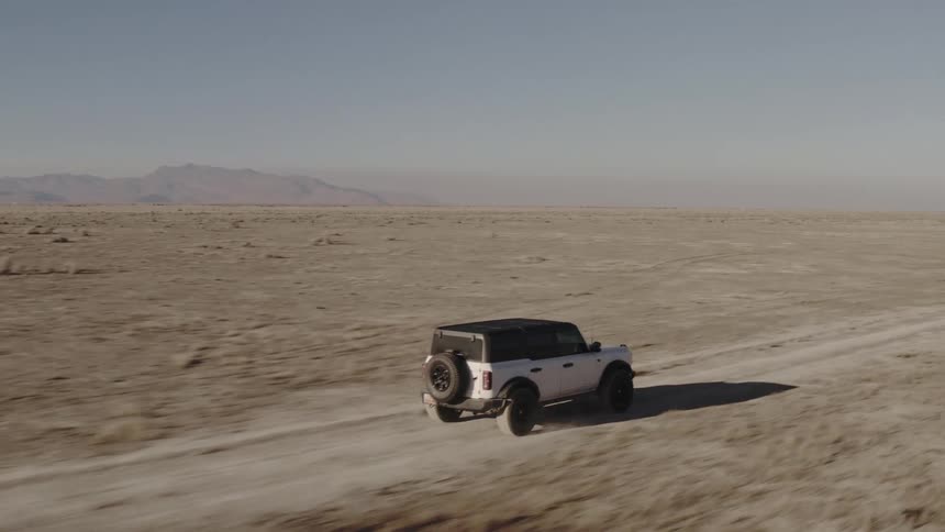Suv drives along a dirt road in an arid region with mountains in the background