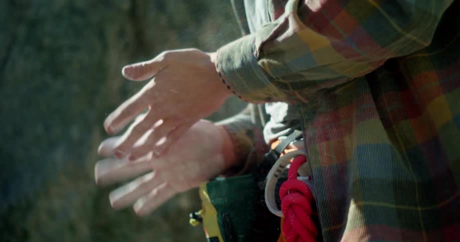 Female rock climber standing near a steep rock wall chalks her hands