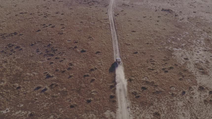 Vehicle drives along a dirt road through an arid landscape