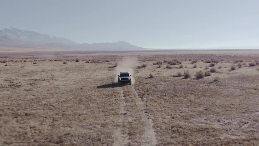 Car drives along a trail across an arid plain with mountains in the background