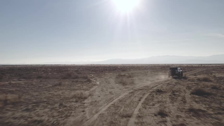 An suv driving in a desert environment releasing dust as it passes by