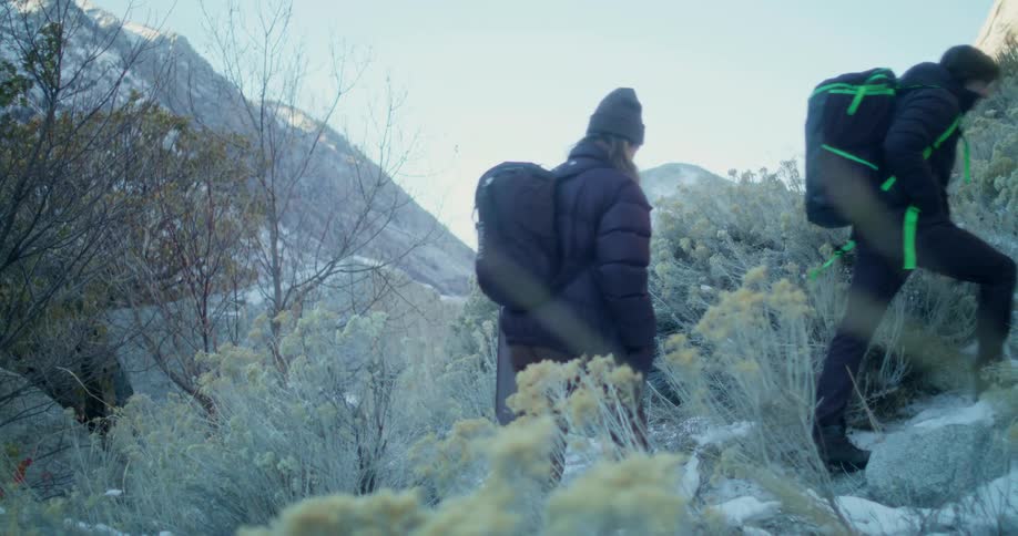 The video shows a man and a woman hiking on a snowcovered rocky hill they both have backpacks on the video has a watermark that reads filmsupply