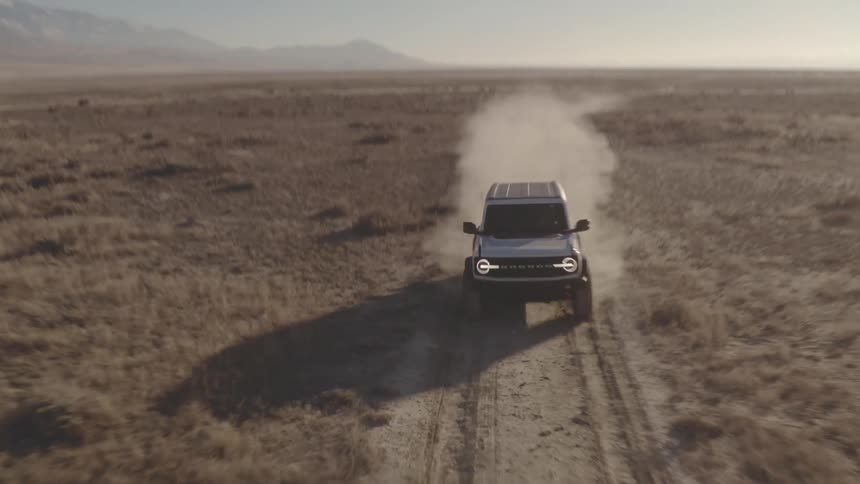 A black suv drives along a dusty trail through a vast barren landscape with distant mountains under a clear sky