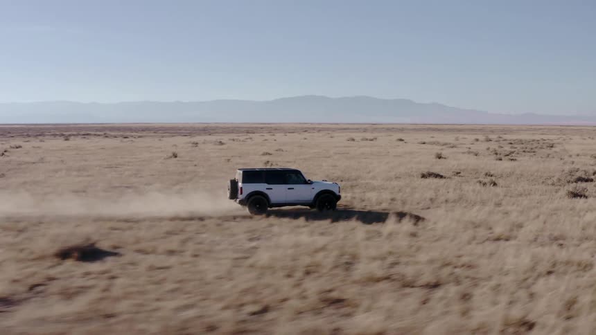 A white suv drives through a desert under a clear sky