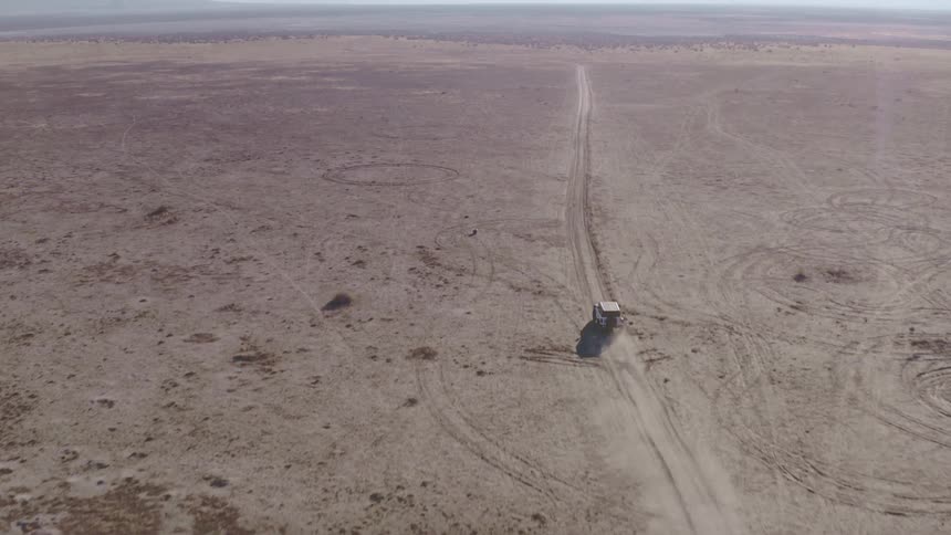 Aerial of jeep driving across wide open desert dirt road