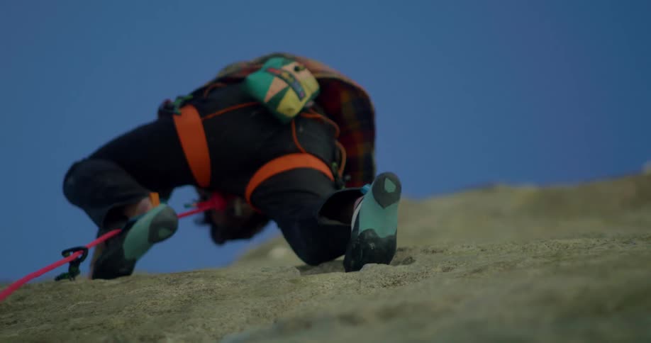 Climber seen from below ascends a rock wall using a safety rope