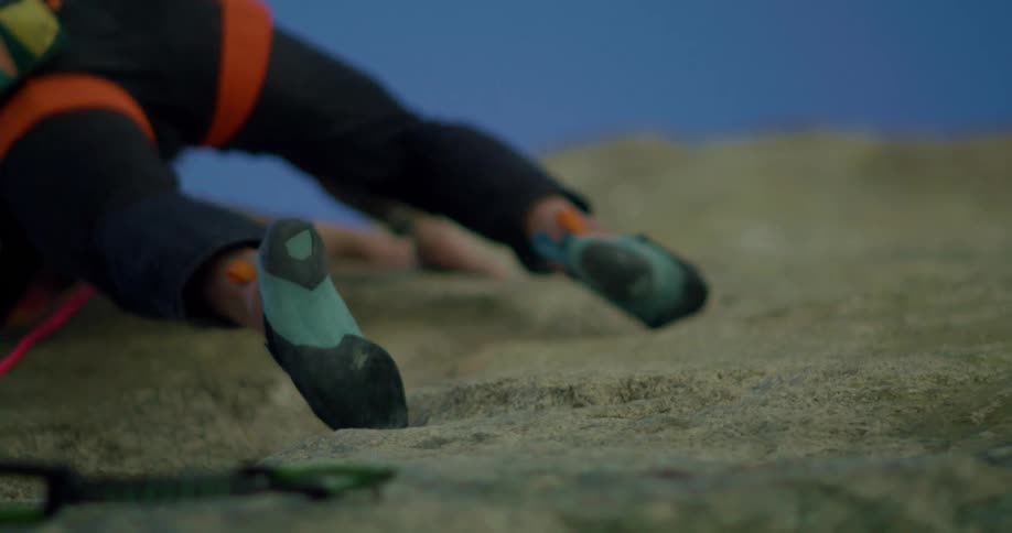 Climber wearing dark blue climbing shoes places feet on small rock holds while ascending