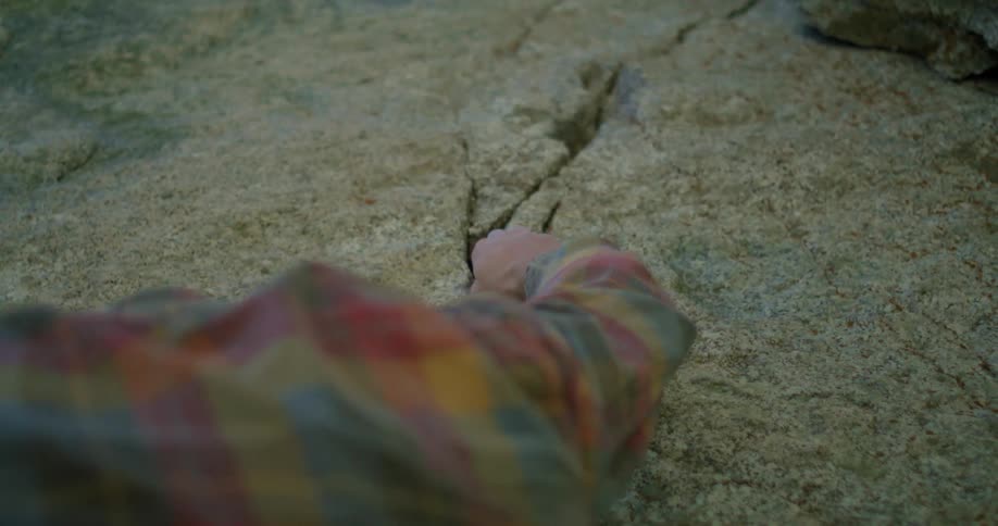 Person climbing rock with hand gripping a crack