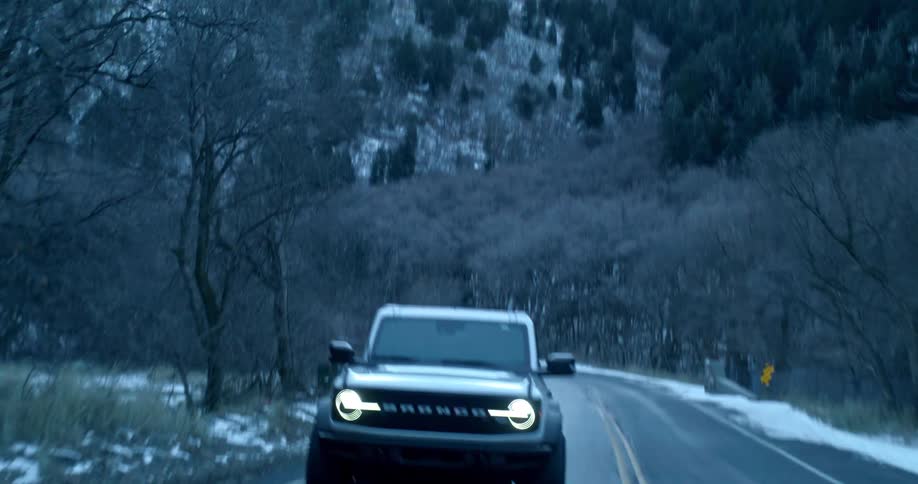 Ford bronco drives on a mountain road with snow on the sides