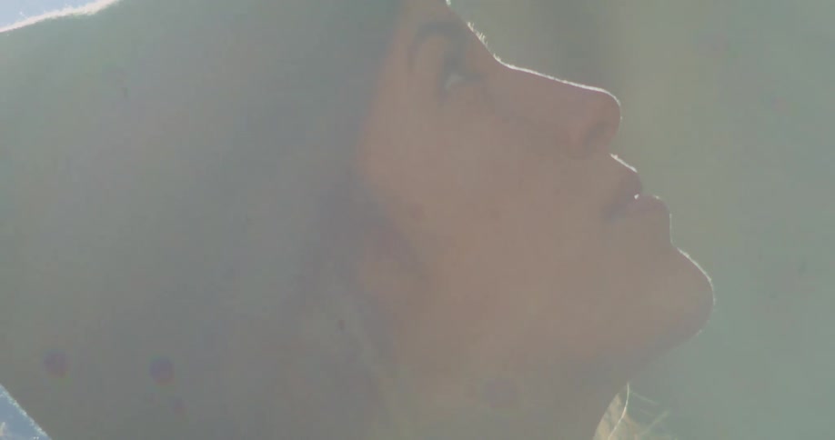 The face of a young woman looking up and wearing a beanie and the sunlight is illuminating her face
