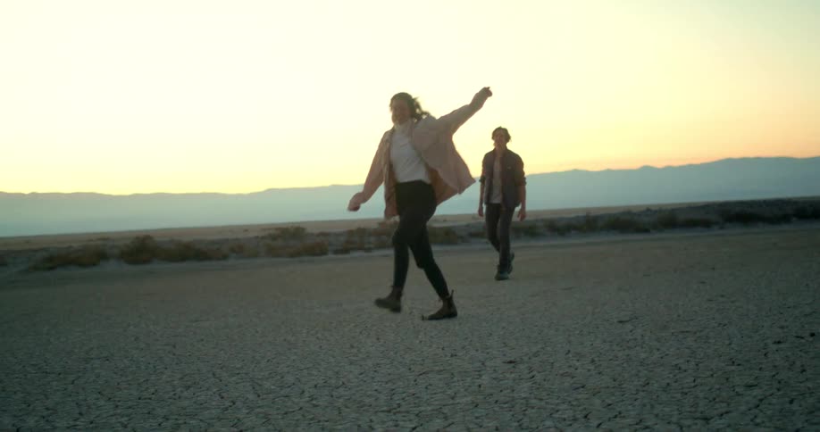 A couple walks playfully through a dry open landscape at sunset