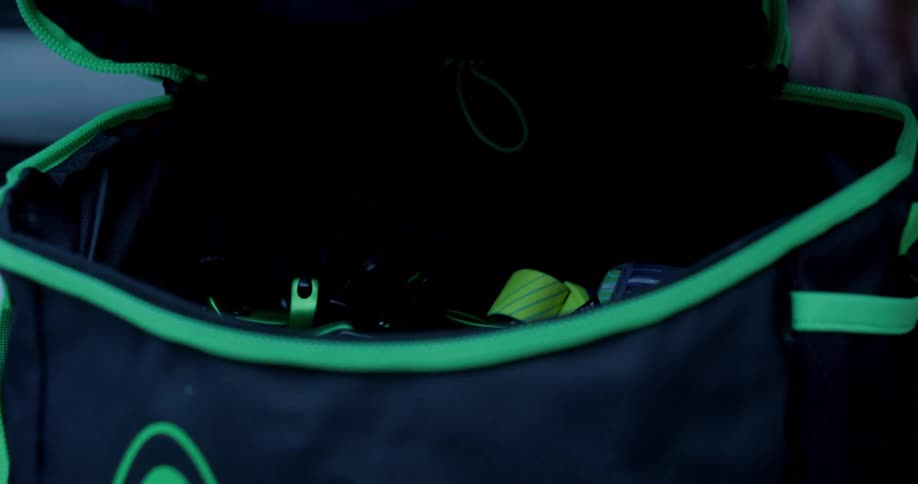 Hand closing black backpack with green details