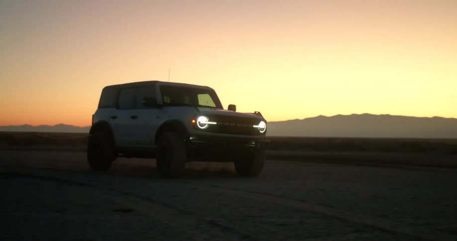 Suv with headlights on parked in a desert area at sunset