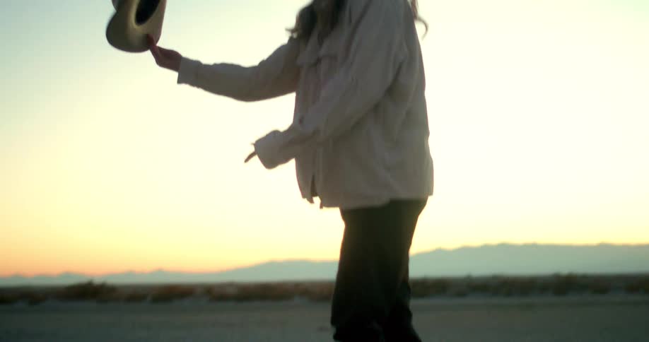 Woman holding a hat while walking at sunset