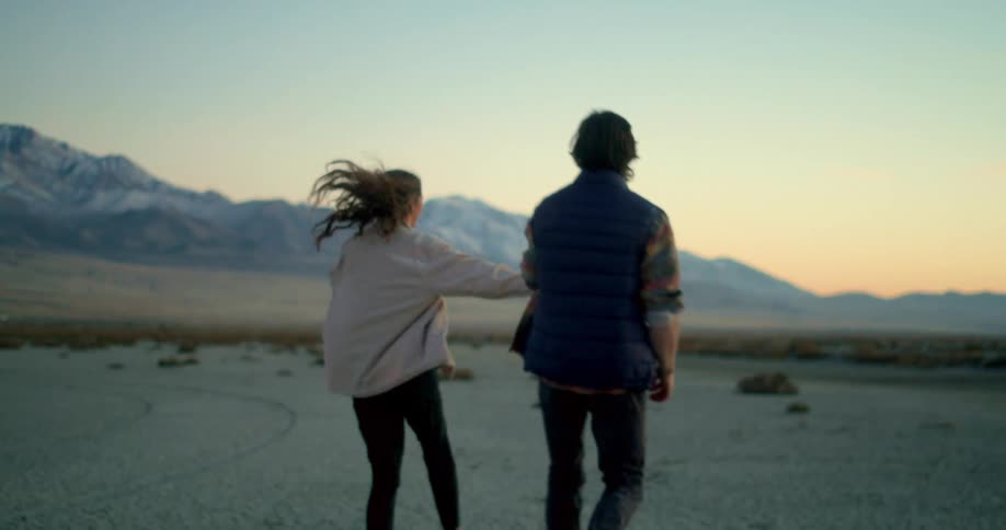 Couple walks smiling on desert plain with snowy mountains in the background