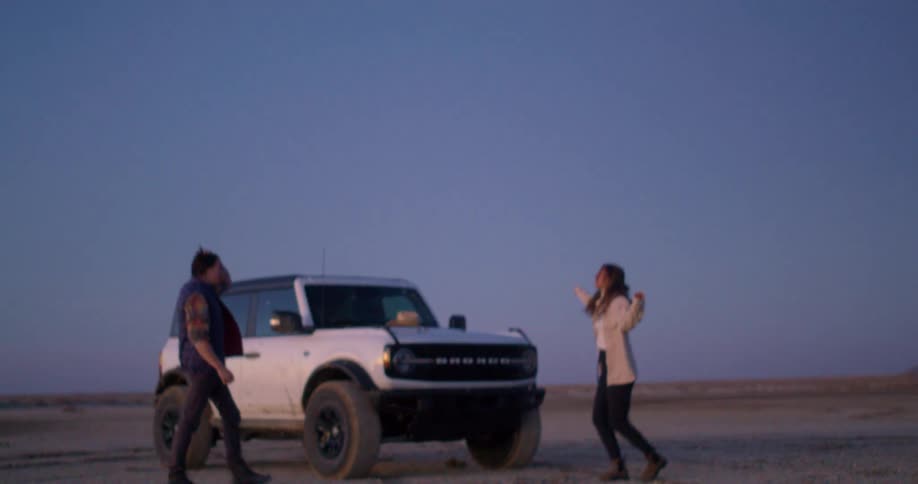Couple interacts with smiles in front of an offroad car at dusk